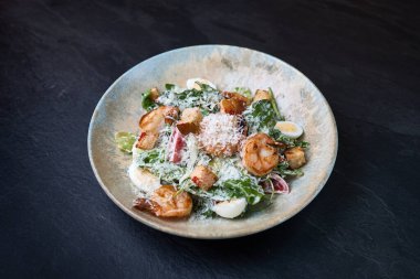 Sağlıklı Sezar salatası üstü ızgara karides, kızarmış kıtır ekmek, tıraş edilmiş parmesan peyniri, yapraklı yeşillikler ve kırsal bir kasede dilimlenmiş yumurta..