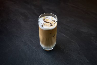 Soğuk buzlu latte, şeffaf bardakta servis edilir. Süt köpüğü ve buz küpleriyle birlikte. Modern, koyu taştan bir yüzeye yerleştirilir..