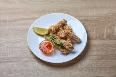 Bir tabak altın ekmekli tavuk şeritleri yanında tatlı biber sosu, taze yeşillikler ve garnitür olarak da limon dilimi..