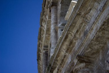 Kolezyumun bir bölümünde, kemer ve sütunlar gibi klasik Roma mimari unsurları sergileniyor. Yapının ihtişamını ve ölçeğini vurgulayarak yukarı doğru bir açıyla çekiliyor..