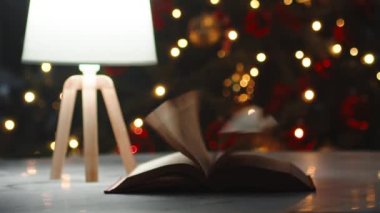 Aydınlatılmış Noel ağacı arkaplanı olan bir masaya göz attığınız kitap