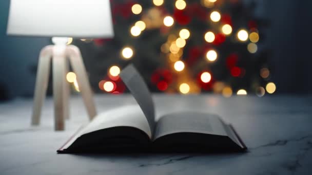 Boek Bladeren Een Tafel Met Verlichte Kerstboom Achtergrond — Stockvideo