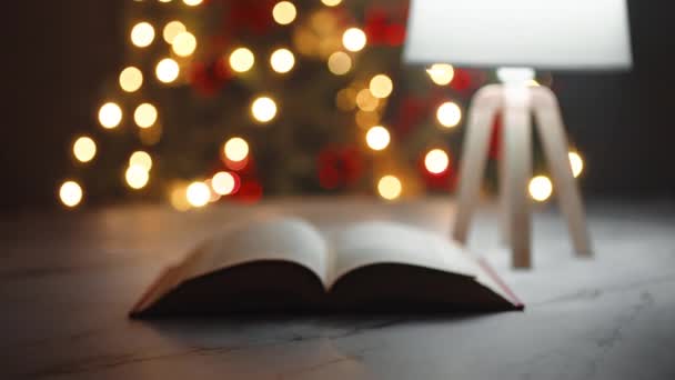 Boek Bladeren Een Tafel Met Verlichte Kerstboom Achtergrond — Stockvideo