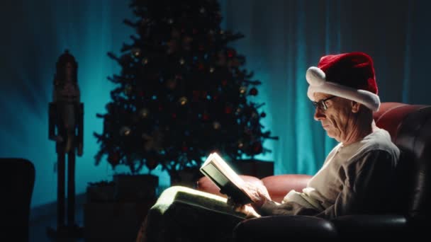 Ηλικιωμένος Άνθρωπος Διαβάζει Βιβλίο Για Χριστούγεννα Καναπέ Στη Νύχτα Ενός — Αρχείο Βίντεο