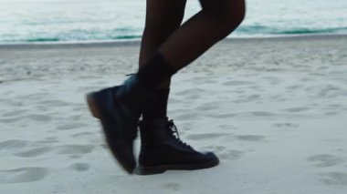 Black boots of a girl walking on the beach