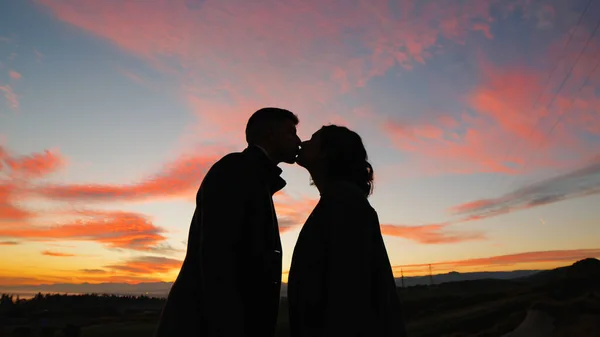 Silhouette of couple kiss against the orange sunset.