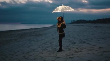 Beautiful girl enjoy the life on the beach near the ocean with a magic glowing umbrella in the night