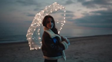 Beautiful girl enjoy the life on the beach near the ocean with a magic glowing umbrella in the night