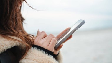 Girl chatting with a smartphone on the beach in overcast winter day.
