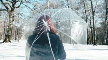 Kız karla çevrili şeffaf bir şemsiyeyi hareket ettiriyor. 