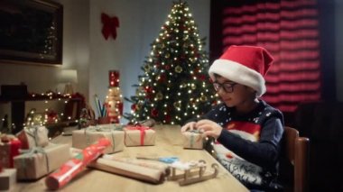 Noel şapkalı çocuk masasında hediyelere bakıyor. . 