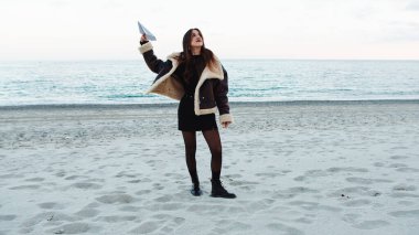Happy girl dancing on the beach near the ocean in winter overcast day.
