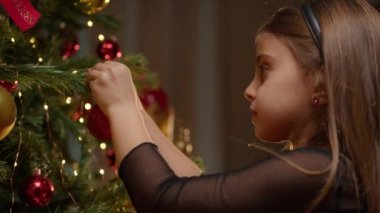 Genç kız Noel ağacını süslemek için kırmızı top koyuyor. . 