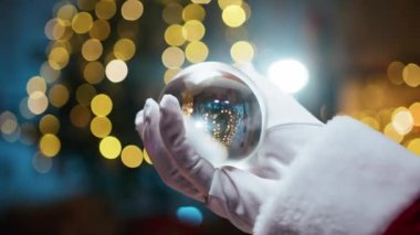 Noel Baba sihirli cam topu Noel ağacına karşı tutuyor.