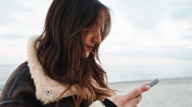 Girl using the smart phone on the beach outdoor overcast day.