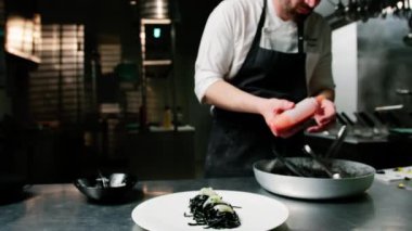 Şef kalamar mürekkepli spagettiye domates sosu koyuyor..
