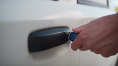 Siyah giyinmiş adam anahtarı beyaz arabaya koyar ve arabaya biner..