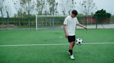 Genç futbolcu futbol topuyla top sürüyor..
