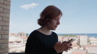 Balkonda telefonunda kısa saçlı mesajlar olan bir kadın..