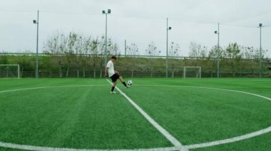 Genç futbolcu futbol sahasının ortasında top sürüyor.