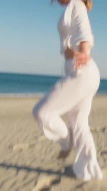 Yazın plajda beyazlar içinde dans eden genç bir kadın.