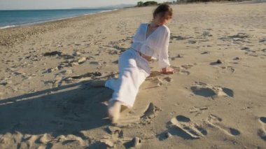 Yazın plajda beyazlar içinde dans eden genç bir kadın.