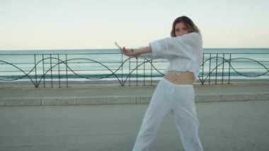 Yazın plajda beyazlar içinde dans eden genç bir kadın.