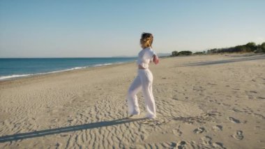 Yazın plajda beyazlar içinde dans eden genç bir kadın.