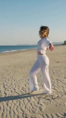 Yazın plajda beyazlar içinde dans eden genç bir kadın.