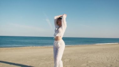 Yazın plajda beyazlar içinde dans eden genç bir kadın.