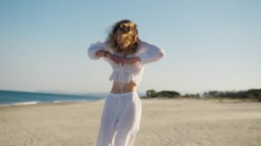 Yazın plajda beyazlar içinde dans eden genç bir kadın.