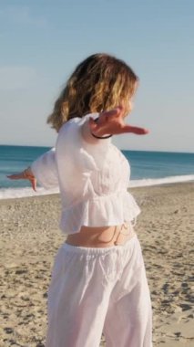 Yazın plajda beyazlar içinde dans eden genç bir kadın.