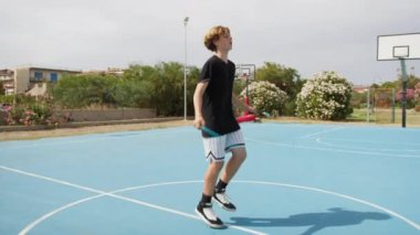 İki genç erkek dışarıda mavi alanda basketbol oynuyorlar..