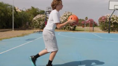 İki genç erkek dışarıda mavi alanda basketbol oynuyorlar..