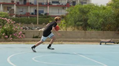 İki genç erkek dışarıda mavi alanda basketbol oynuyorlar..
