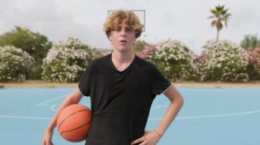 İki genç erkek dışarıda mavi alanda basketbol oynuyorlar..