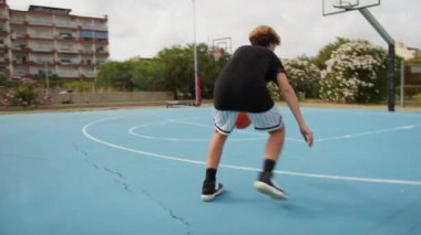 İki genç erkek dışarıda mavi alanda basketbol oynuyorlar..