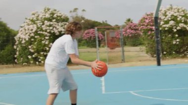 İki genç erkek dışarıda mavi alanda basketbol oynuyorlar..