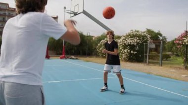 İki genç erkek dışarıda mavi alanda basketbol oynuyorlar..