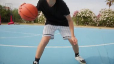 İki genç erkek dışarıda mavi alanda basketbol oynuyorlar..