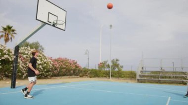 İki genç erkek dışarıda mavi alanda basketbol oynuyorlar..