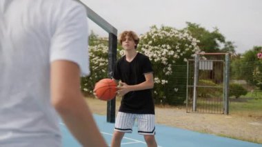 İki genç erkek dışarıda mavi alanda basketbol oynuyorlar..