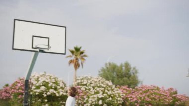 İki genç erkek dışarıda mavi alanda basketbol oynuyorlar..