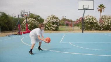 İki genç erkek dışarıda mavi alanda basketbol oynuyorlar..