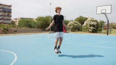 İki genç erkek dışarıda mavi alanda basketbol oynuyorlar..