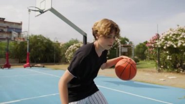 İki genç erkek dışarıda mavi alanda basketbol oynuyorlar..