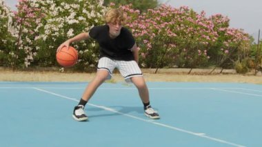 İki genç erkek dışarıda mavi alanda basketbol oynuyorlar..