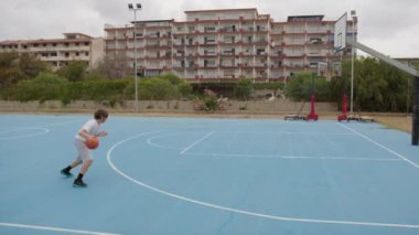 İki genç erkek dışarıda mavi alanda basketbol oynuyorlar..