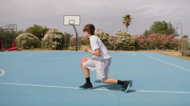 İki genç erkek dışarıda mavi alanda basketbol oynuyorlar..