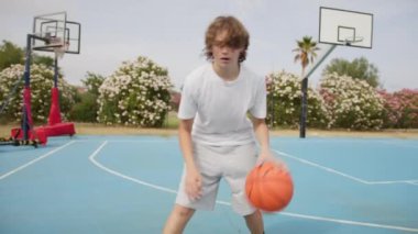 İki genç erkek dışarıda mavi alanda basketbol oynuyorlar..